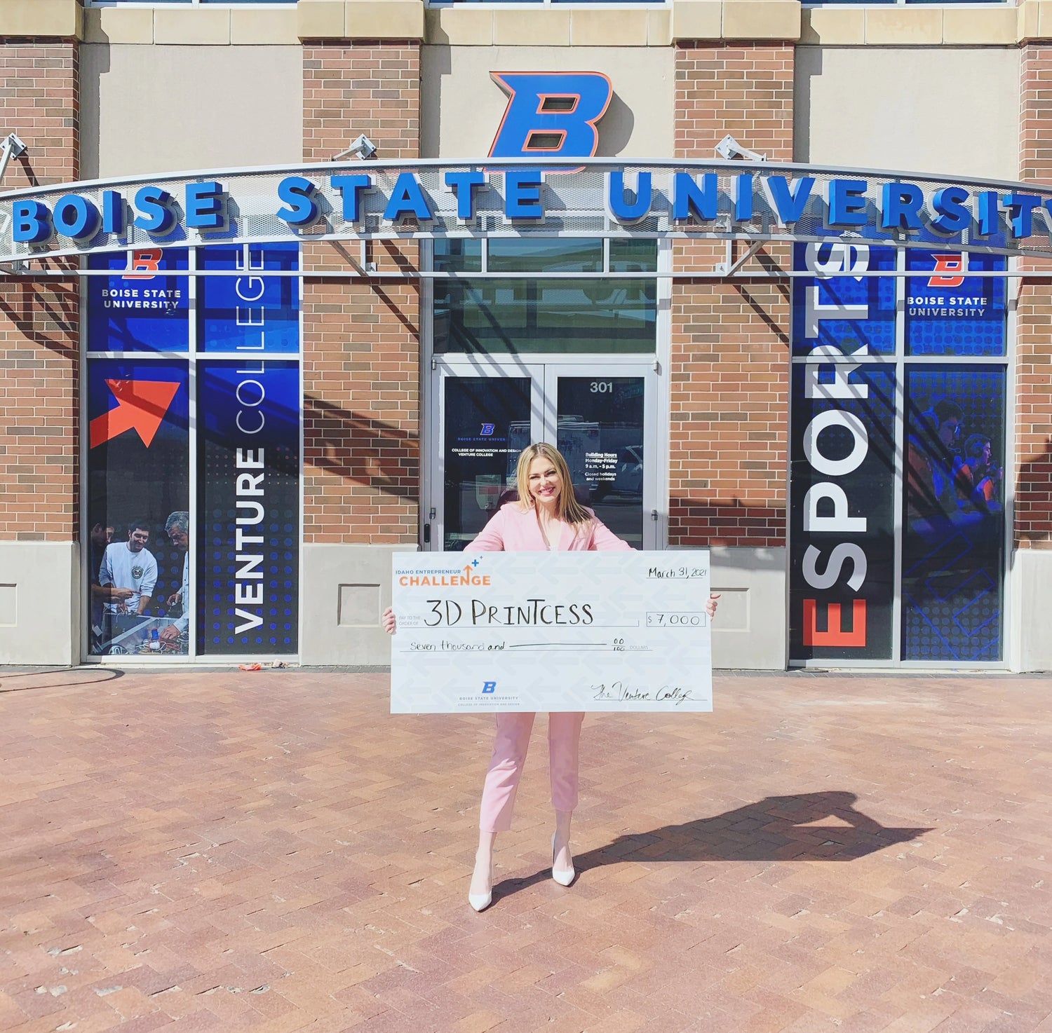 Sierra in front of a Boise State building holding a giant check made out to 3D Printcess after winning her track of the Idaho Entrepreneur Challenge.