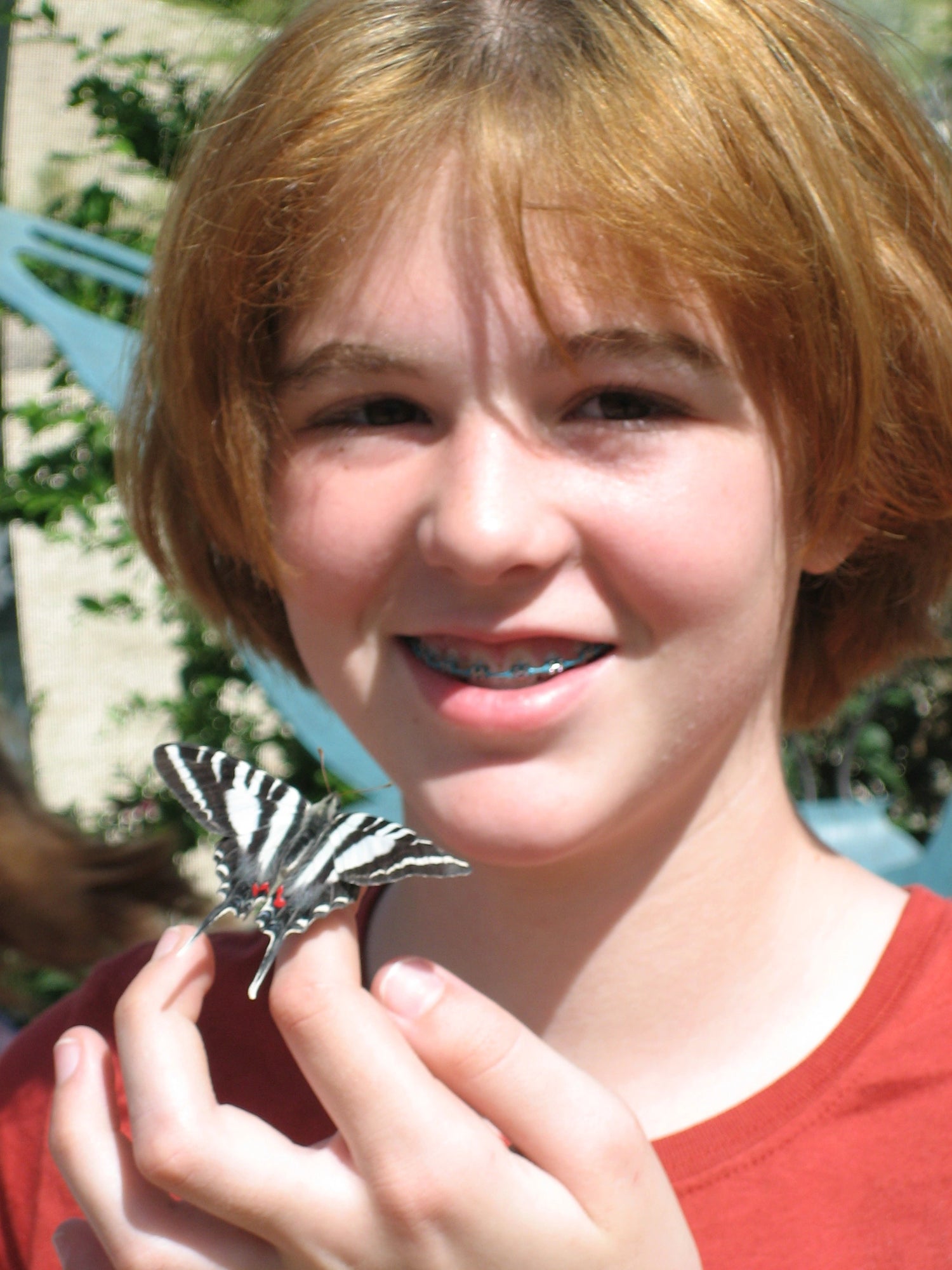 6th grade Sierra holding a butterfly at an insect exhibit. She has braces, severely unwaxed eyebrows, and very short, bright orange hair after a middle school hair crisis that still haunts her to this day. 